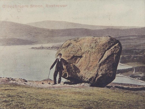 Photographic postcard of a walker at the “Big Stone”, Cloughmore, overlooking Carlingford Lough, Warrenpoint and the Ross Monument. Newry & Mourne Museum Collection