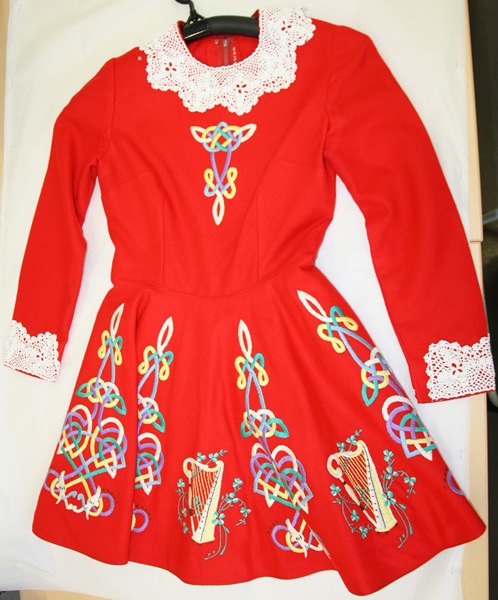 This hand-embroidered dress and brat—a folded cloak worn over the shoulder—were worn by Sheila Nolan when she won the All-Ireland and International Irish Dancing Championship in 1971. The intricate designs and motifs are inspired by the Book of Kells, while the collar and cuffs feature hand-crocheted rose and shamrock patterns. Sheila trained at the Arthur Burns School of Irish Dancing in Newry. Newry and Mourne Museum Collection