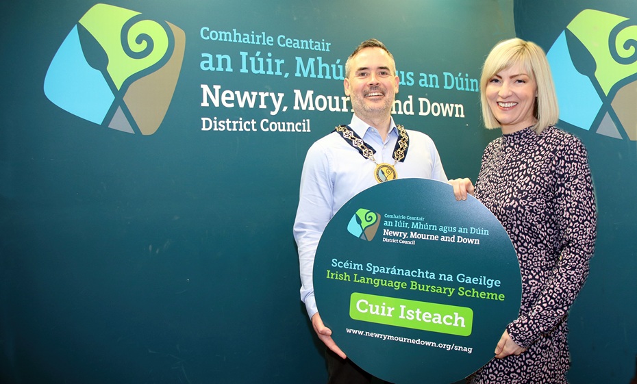 Tá Gairm 1 de Scéim Sparánachta na Gaeilge 2026-2027 seolta ag Cathaoirleach Chomhairle Ceantair an Iúir, Mhúrn agus an Dúin, an Comhairleoir Pilib Mac Cathmhaoil agus Bainisteoir Aonad na Gaeilge, Louise Smith. Cuideoidh an scéim le daoine a bhfuil cónaí orthu i gceantar na Comhairle freastal ar choláistí agus ar chúrsaí Gaeilge trí sparánacht a chur ar fáil chun cuidiú le táillí agus costais chúrsa a chlúdach.  - Newry, Mourne and Down District Council Chairperson, Councillor Philip Campbell and Irish Language Unit Manager, Louise Smith launch Call 1 of the Council’s Irish Language Bursary Scheme 2026-2027. The scheme will help residents in the district to attend Irish Language colleges and courses through bursary assistance aimed at covering course costs and fees. 