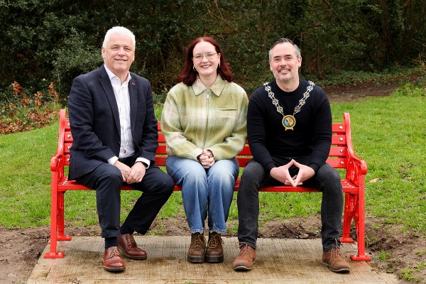 Caoimhe Loughran from Newry at the British Heart Foundation bench installed in living tribute to Caoimhe, who had a pacemaker fitted at just 20 years of age, due to an underlying heart condition. Pictured alongside Caoimhe is Fearghal McKinney, Head of British Heart Foundation NI, and Newry, Mourne and Down District Council Chairperson, Councillor Philip Campbell. The iconic red bench is situated in the picturesque Kilbroney Park in Rostrevor.