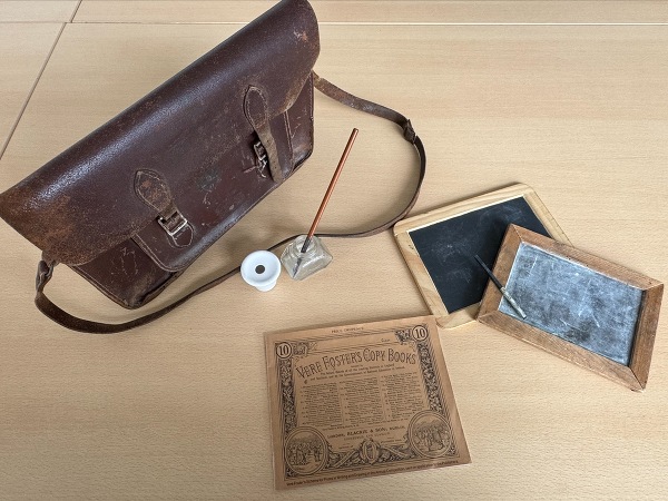 Items from the School life Reminiscence Loan Box consisting of school satchel, ink wells, nib pen, slates, lead pencil and a replica of the Vere Foster Copy Book.  Newry and Mourne Museum Collection