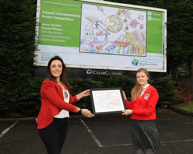 Newry, Mourne and Down District Council Chairperson Councillor Cathy Mason presenting Junior Section winner Effie McMullan from Sacred Heart Primary School, Dundrum with a framed copy of her poster in front of the billboard displaying her winning design. Newry, Mourne and Down District Council Chairperson Councillor Cathy Mason presenting Junior Section winner Effie McMullan from Sacred Heart Primary School, Dundrum with a framed copy of her poster in front of the billboard displaying her winning design.