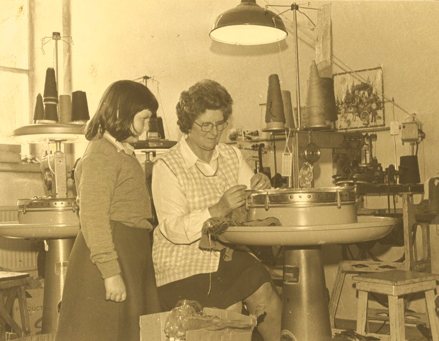 A pupil from Kilkeel Primary School watching one of the employees at the Kilkeel Knitting Factory at work during a school visit to the factory in 1979. Newry and Mourne Museum Collection