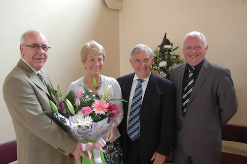 Mrs Josephine Conlon, accompanied by her husband Mr Leo Conlon, is presented with flowers by Principal of St Paul’s High School, Mr Oliver Mooney to mark her retirement from the school.  (also present is Head of Learning Support Centre at St Paul’s, Mr Paddy McAvoy).